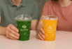 Two cold juice cups, one green from Dietta and one orange from Summit Juice, held by two people.