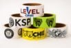 Pyramid stack of colorful custom packaging tapes with bold logos, including pet products, lingerie, and technical services.