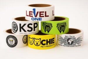 Pyramid stack of colorful custom packaging tapes with bold logos, including pet products, lingerie, and technical services.
