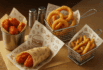 Premium custom basket liner paper featuring burger and veggie illustrations, used with buffalo bites, onion rings, and seasoned fries in metal baskets.