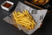 Custom newsprint-style basket liner holding golden French fries served with ketchup in a modern black setting.