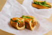 Premium custom food wrapping paper with a charming chef illustration and vegetable-themed patterns, used to wrap a fresh banh mi sandwich filled with shredded pork and pickled vegetables — perfect for stylish and eco-friendly food presentation.