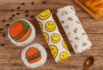 Premium custom food wrapping paper featuring creative burger, smiley face, and croissant-themed designs, elegantly wrapped around various food items on a rustic wooden surface — ideal for gourmet branding and takeout packaging.