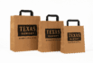 Three kraft paper bags of different sizes featuring Texas Hungry Barbecue & Grill branding on a white background.