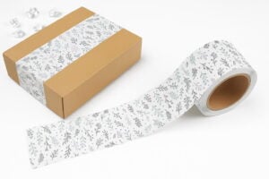 Decorative tape with floral patterns sealing a kraft box, paired with a matching roll of tape on a clean white background.